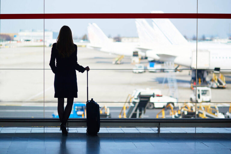 woman with luggage looking at plane through airport windows