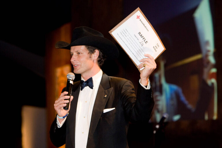committee chairman conducting raffle on stage at British Red Cross London Ball Honkey Tonk Blues country music themed fundraising event
