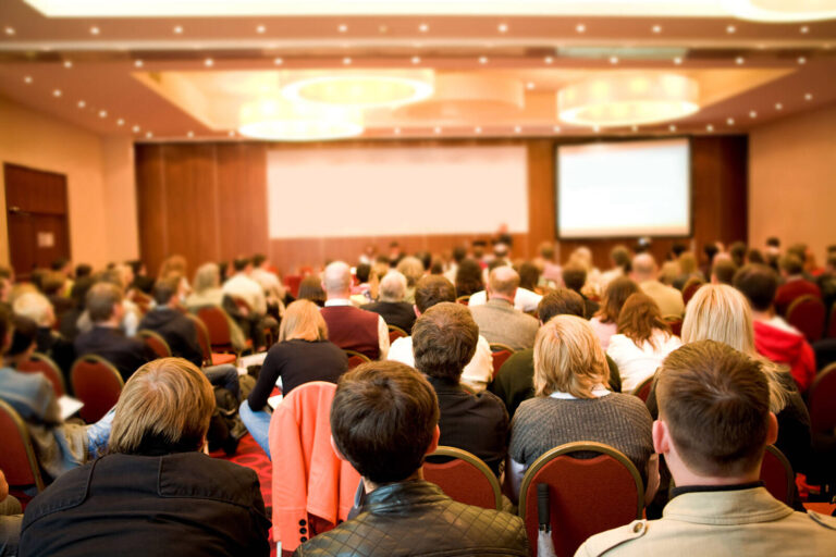 crowded meeting room filled with people watching a presentation