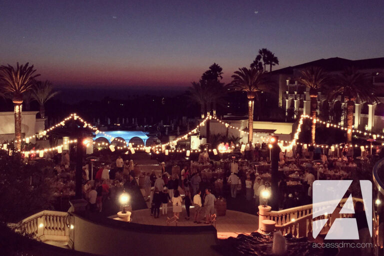 people at dinner tables with string lighting overhead at an outdoor evening event