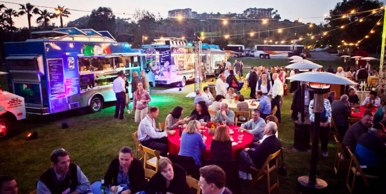 people at dinner tables next to food trucks at an outdoor event