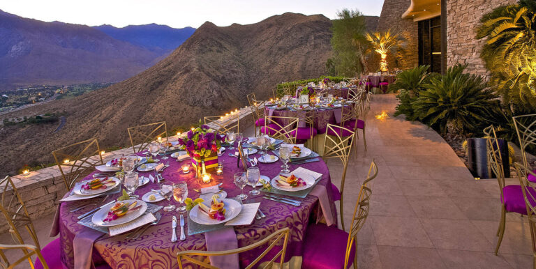 purple linen covered dinner tables set up on a dessert mountain range