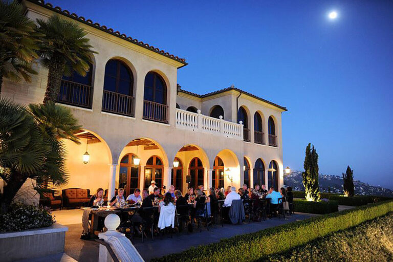 people eating at dinner tables set up on a terrace outside a villa a night