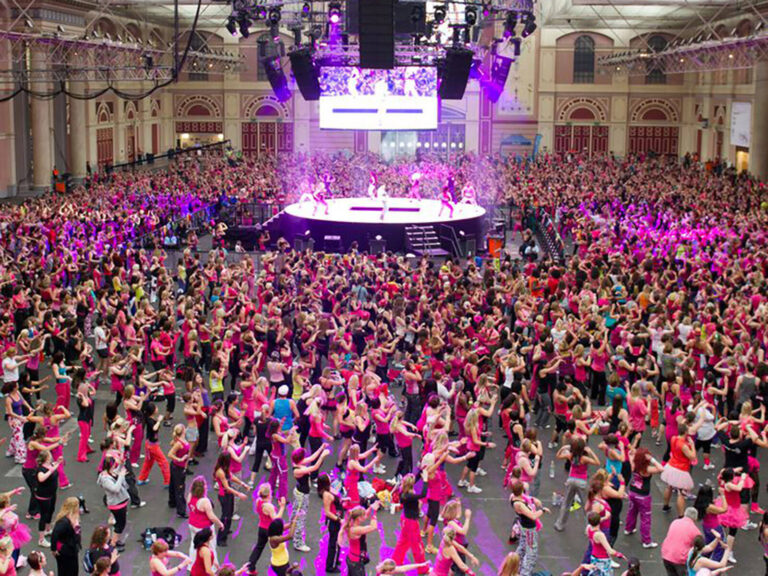 hundred of people wearing pink dancing in an exhibition hall for the Zumba Party in Pink